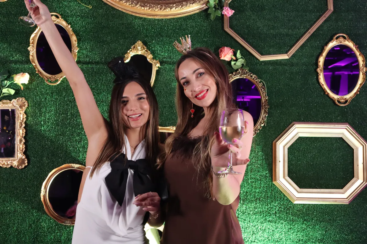 Two guests celebrating at event photography station with styled green and gold backdrop