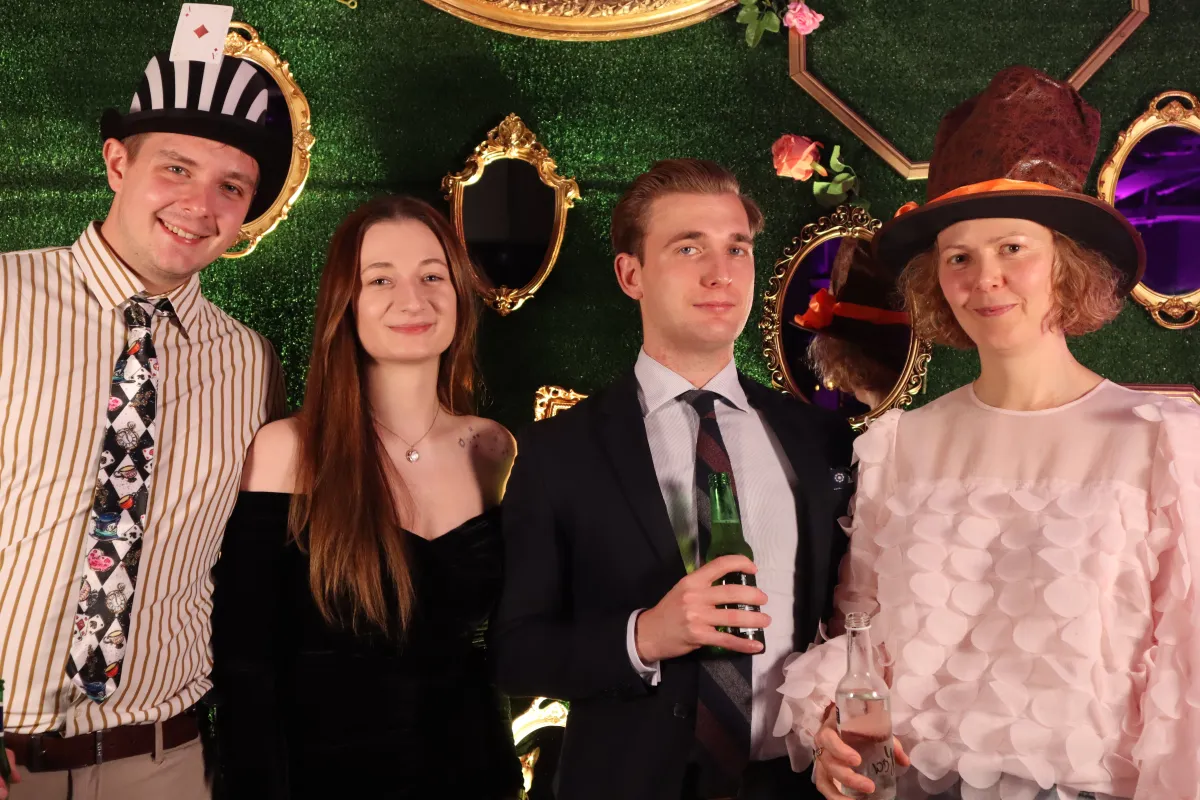 Group of four guests with props posing for professional event photographer with ornate backdrop